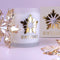 A frosted glass candle jar with a metallic gold snowflake cutout and the word 'WINTERGOLD' printed below, styled on a pale lavender surface with decorative crystal snowflakes and a matching box in the background.