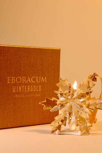 Gold crystal snowflake ornament in front of an Eboracum Wintergold box on a beige background